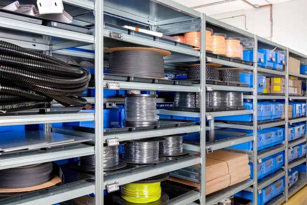 工业仓库货架上摆放着大型电缆卷轴、管材和蓝色储物箱,整齐排列在金属架上。