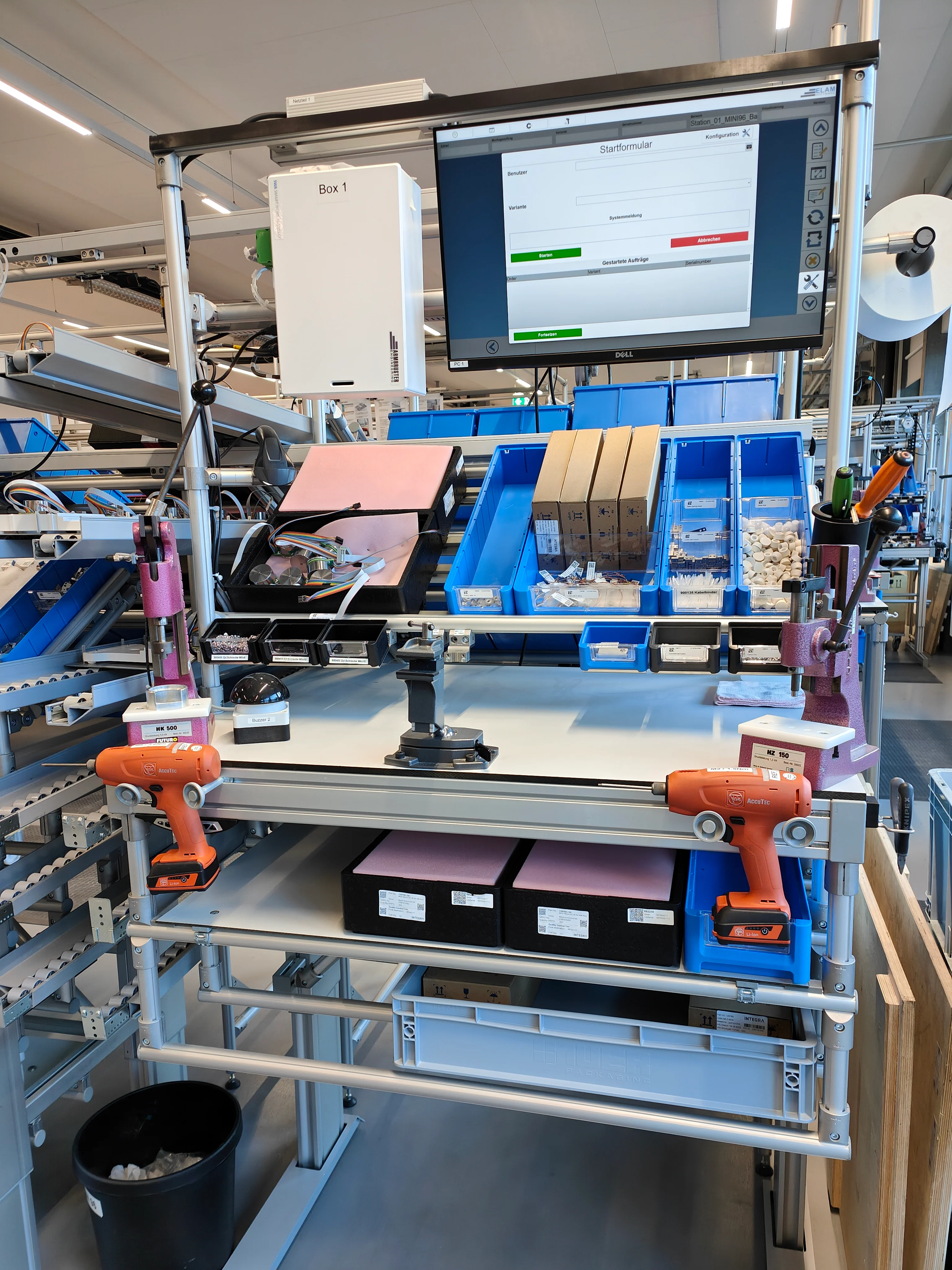 一台电脑屏幕放在工厂现代工作站的桌子上，旁边有工具。